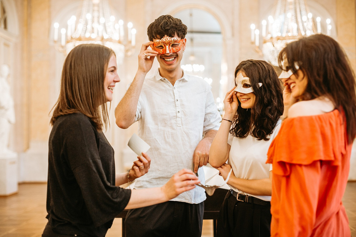 Eine Freundschaftsgruppe, zum Teil mit einer Maske über den Augen - alle lächelnd. Eine Frau hat ein Stück Papier in der Hand. | Foto © Mystery Makers/Philipp Lipiarski