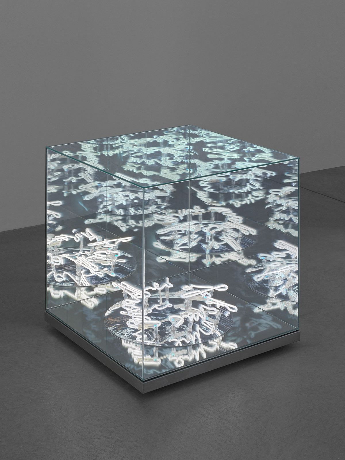 A glass cube containing luminous white abstract lettering.