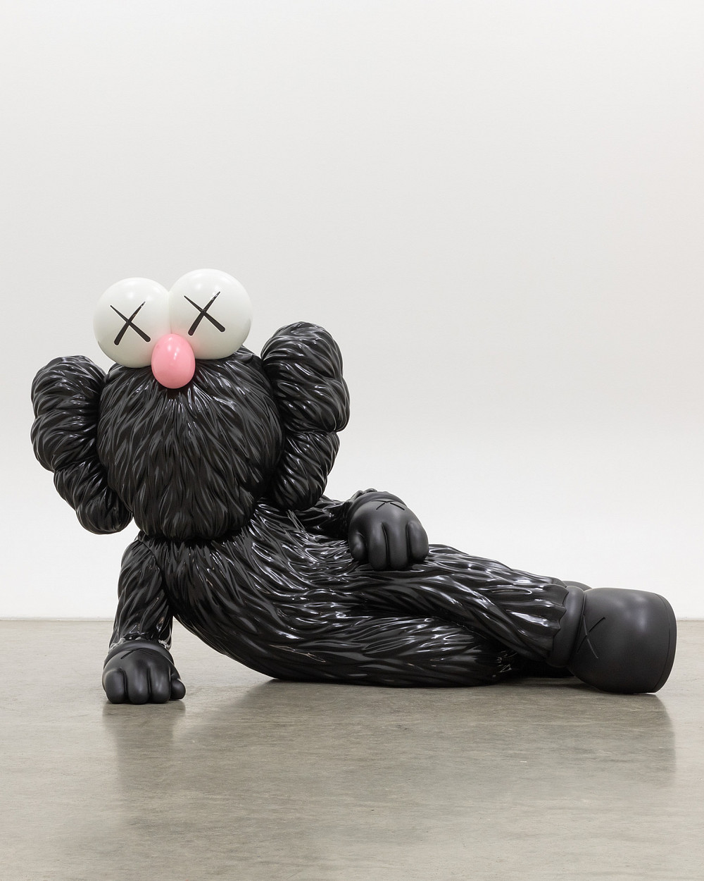 Sculpture of a comic character lying on its side, supported on one side, with black fur, a pink snub nose, and X-shaped eyes.