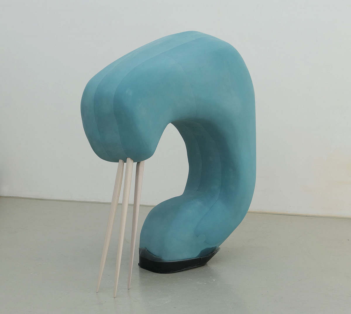 Eine blaue, dicke Skulptur halbrund geformt. Am oberen Ende sind Holzstäbe angebracht, die bis zum Boden reichen und ein spitzes Ende haben, ähnlich wie Zahnstocher.