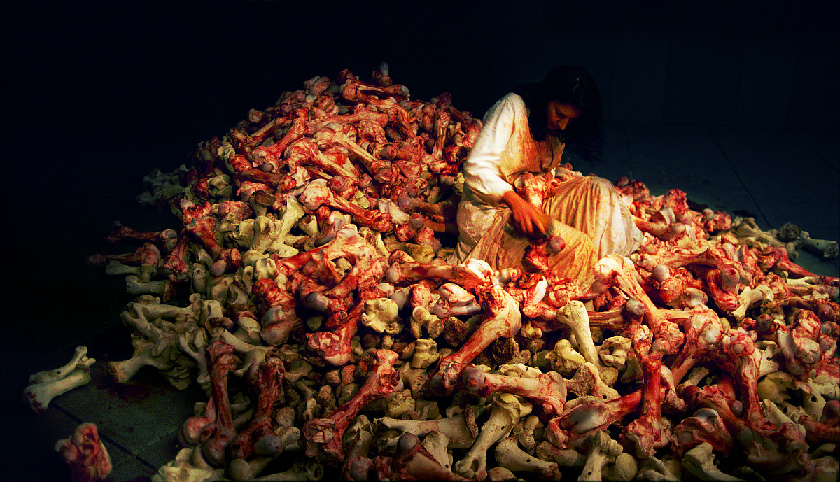 Marina Abramović sits in a white dress on a pile of bloodstained cattle bones and slowly cleans them with a brush; she looks exhausted and concentrated.
