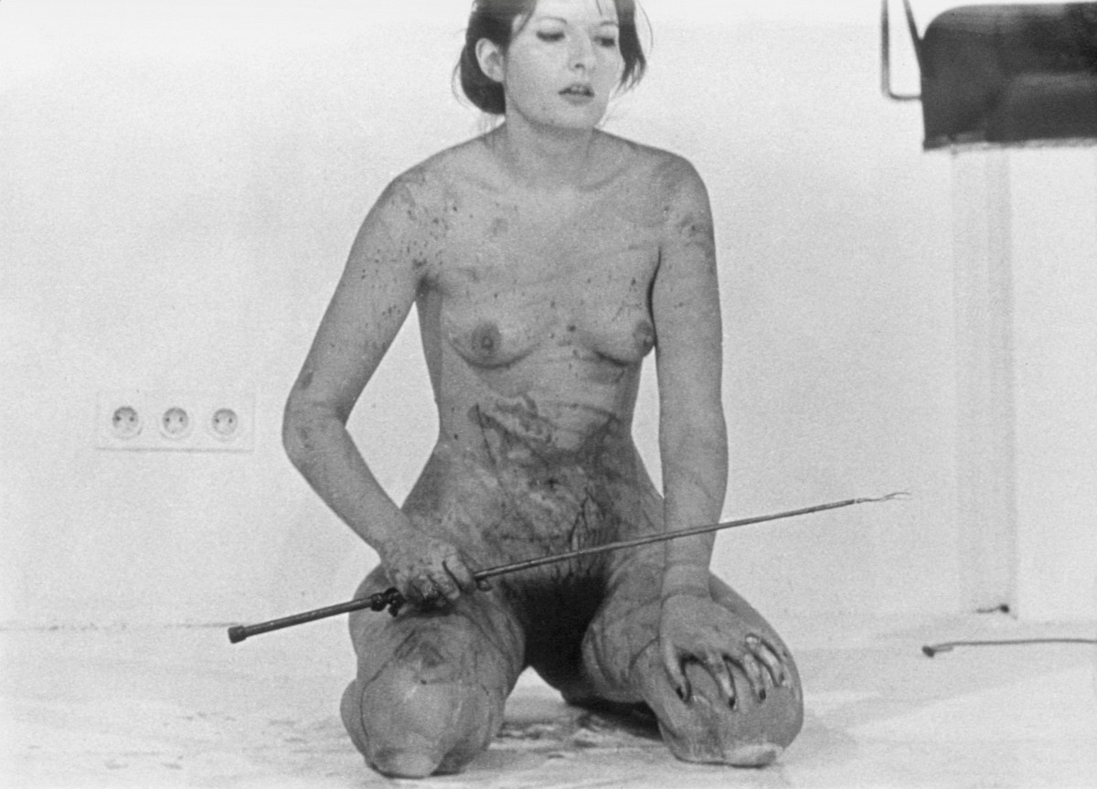 Marina Abramović kneels naked and covered in blood on the floor. A five-pointed star is carved into the skin on her stomach and she is holding a sword in her hand.