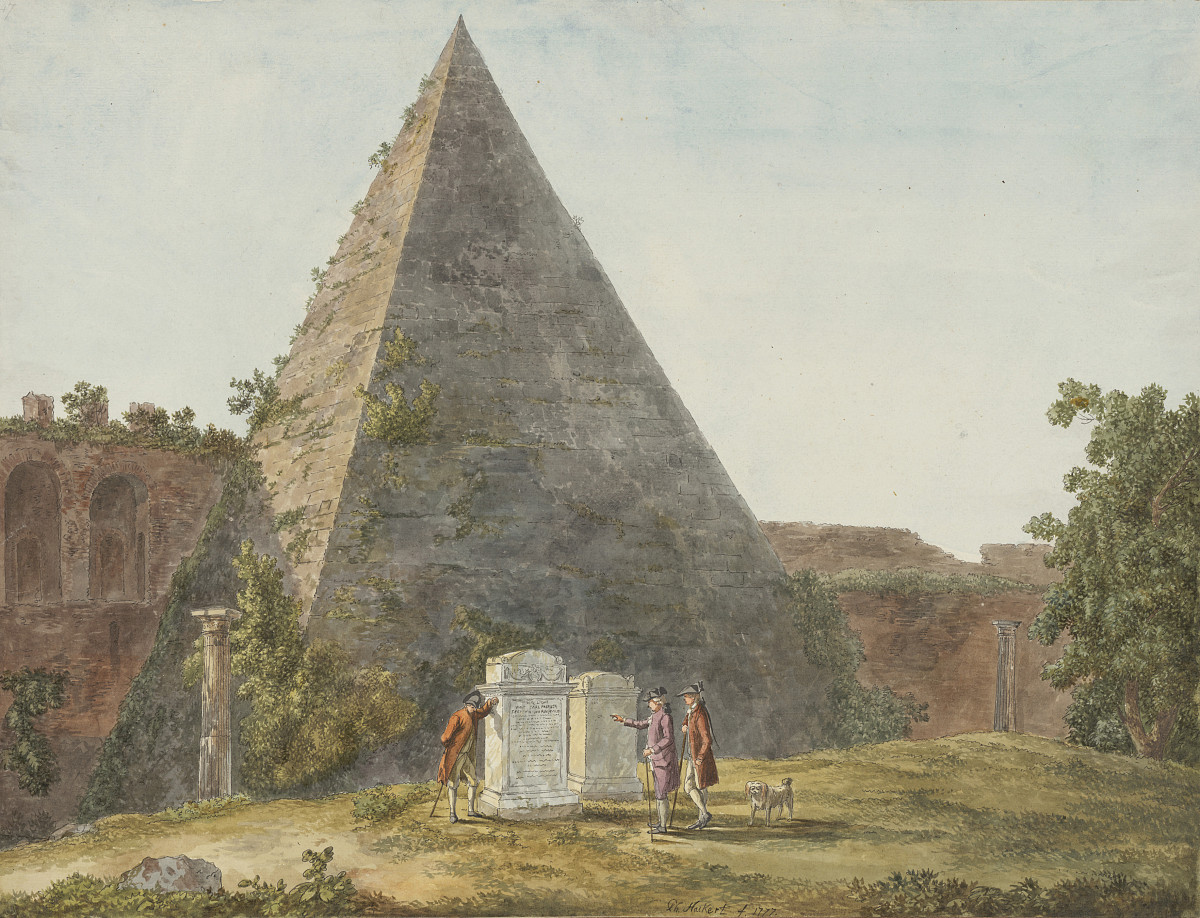 A small pyramid on a hill. The pyramid is partly overgrown with plants. In front of it are two white gravestones and three people with a dog reading the inscriptions. A building with large, arched windows can be seen in the background.