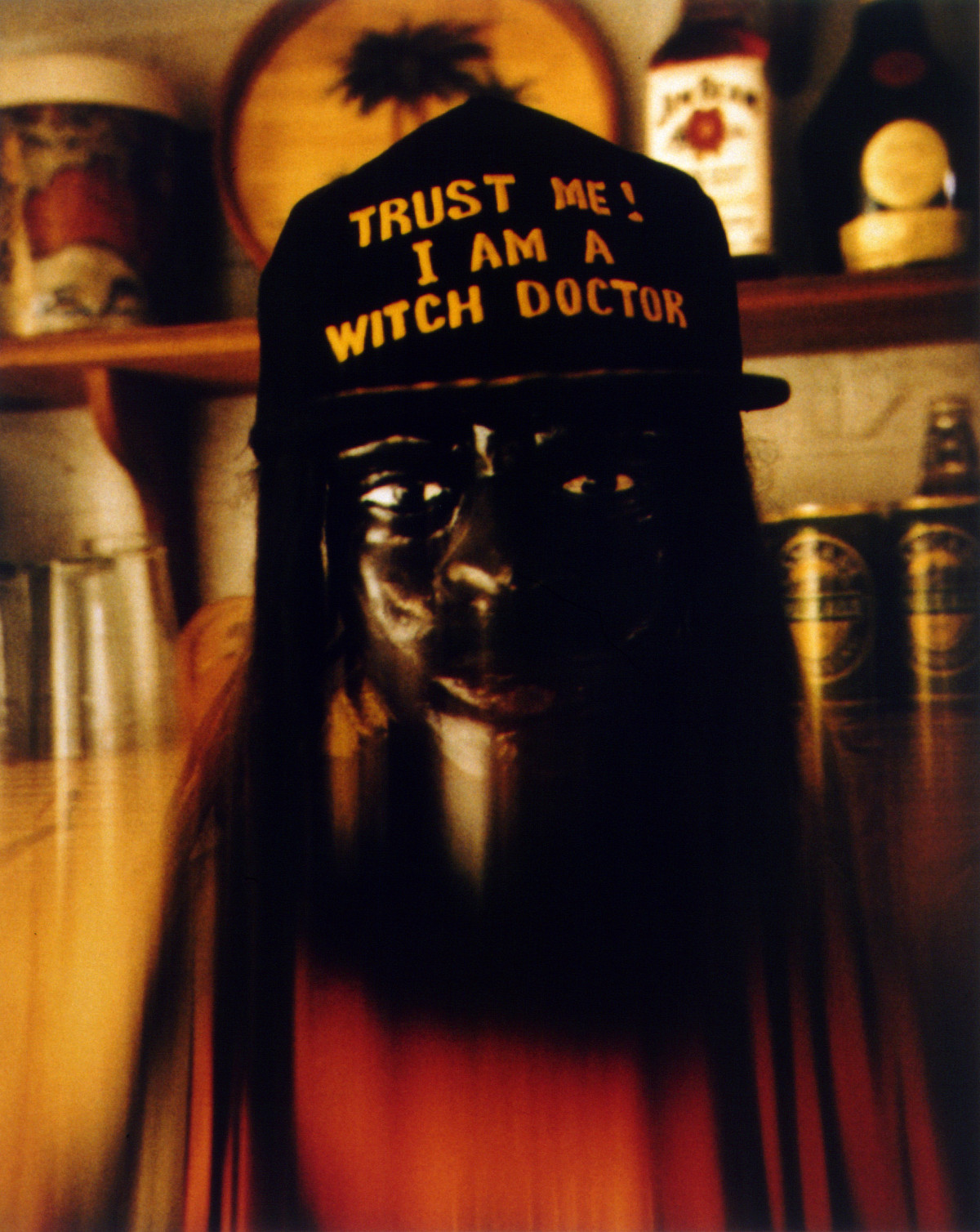 Photograph of a mask that looks like a face, wearing a cap with the inscription “Trust me! I am a witch doctor.”