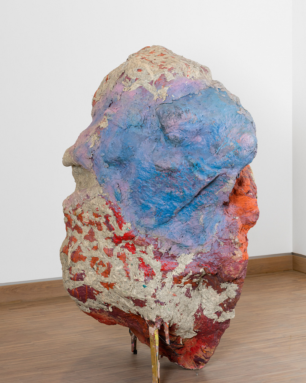 Sculpture in the form of a large stone standing on wooden boards and painted in shades of red and blue.