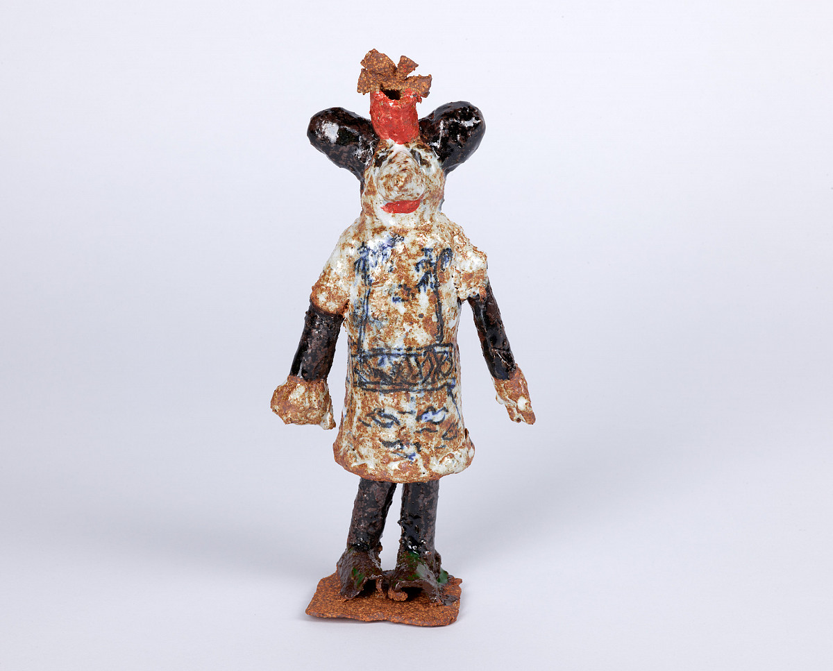 Sculpture of a mouse-like, standing figure with a red hat and blue patterned robe.