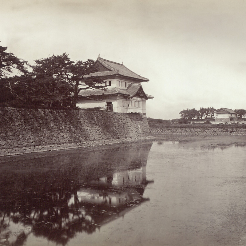 Black-and-white photograph of a Japanese-style guardhouse on the edge of the moat, surrounded by trees.
