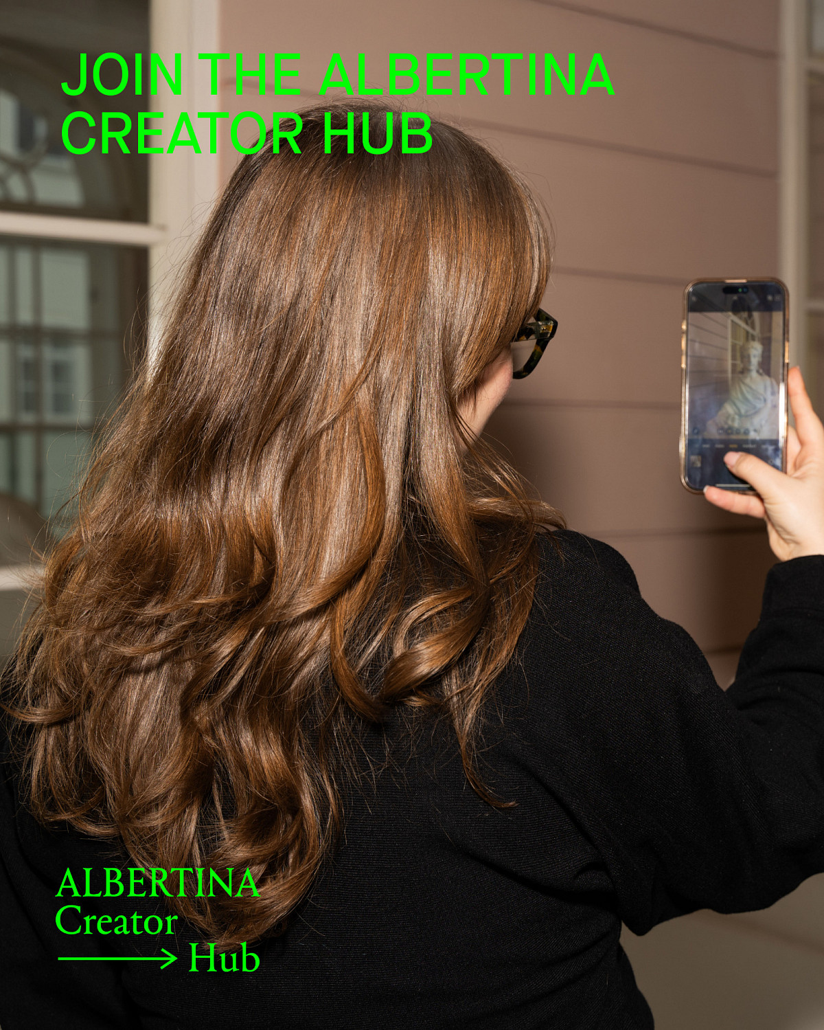 A woman with long curly hair holds a smartphone in her hand and takes a photo of a sculpture in the museum. The image contains the text: "Join the ALBERTINA Creator Hub" and below it is the Creator Hub logo.