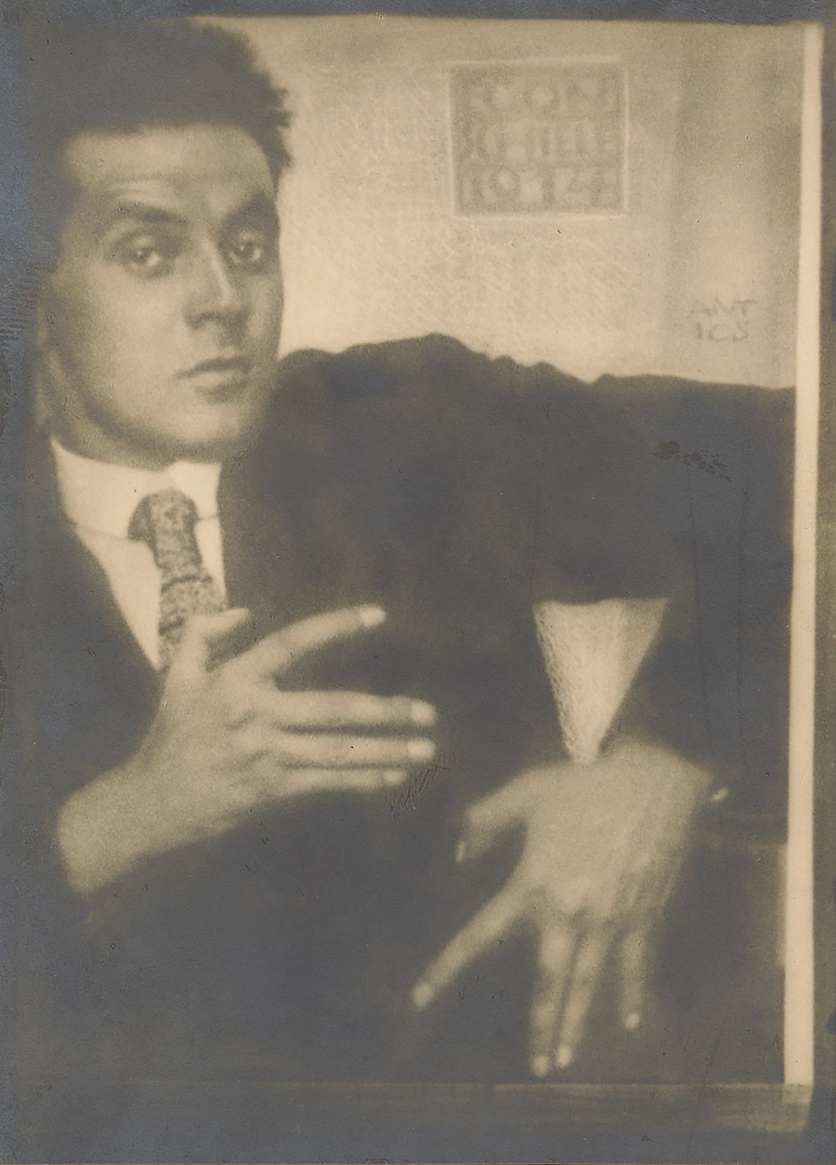 Black-and-white photograph of Egon Schiele holding his hands in front of his chest with his fingers spread apart.