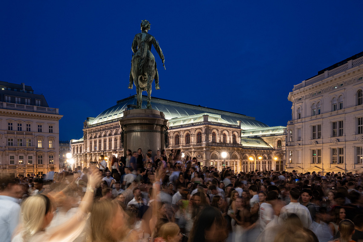Die Bastei der ALBERTINA am Abend mit Blick auf die beleuchtete Oper und vielen tanzenden Menschen unterhalb der Reiterstatue.