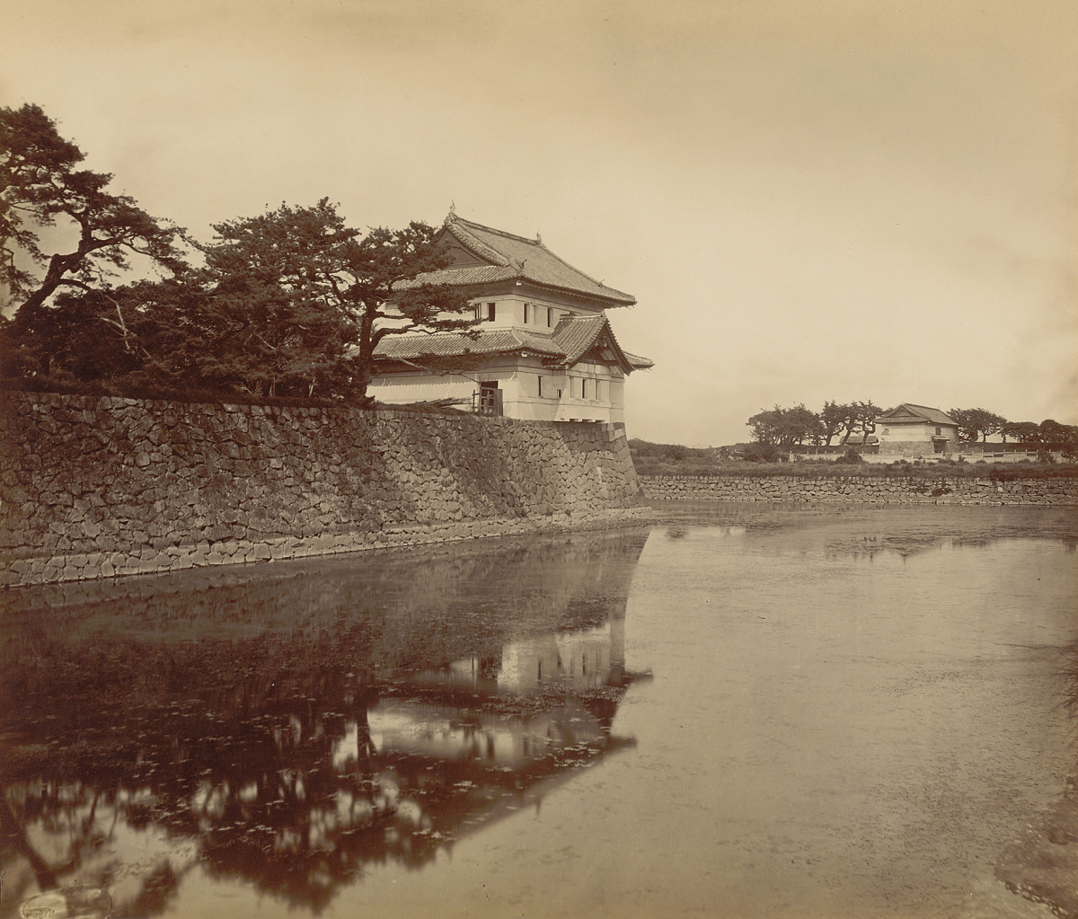 Black-and-white photograph of a Japanese-style guardhouse on the edge of the moat, surrounded by trees.