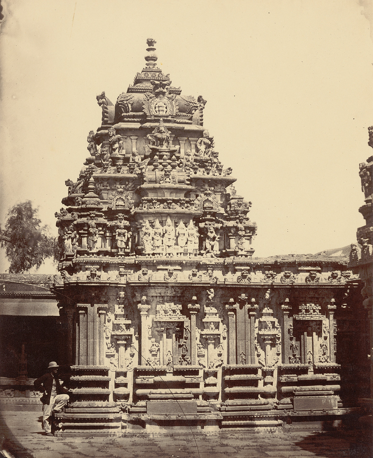 An elaborately decorated temple structure with stone columns, sculpted reliefs, and a person in the foreground.