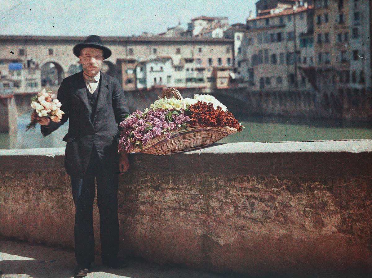 A flower vendor in front of the Ponte Vecchio, with the bridge and other people in the background
